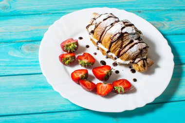 Lezzetli kahvaltı taze kruvasanlar ve mavi ahşap zemin üzerine taze çilek ile