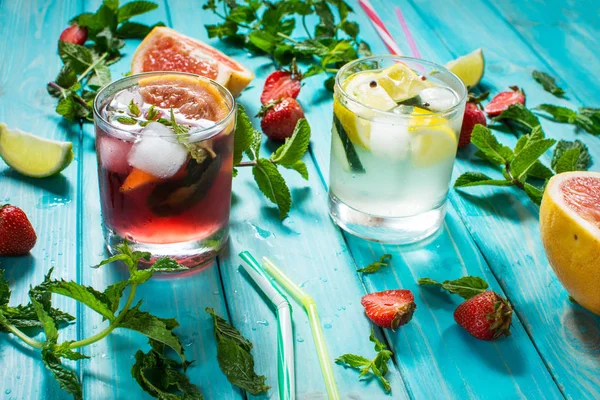 Alkol soğuk kokteyl bardak buz, meyve ve ahşap masa üzerinde kalan nane ile dekore edilmiştir. Limon, çilek, kireç zemin üzerine taze meyve suyu