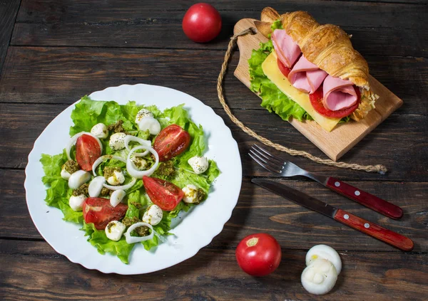 Jarní lehké a vydatné snídaně. Croissant se šunkou, sýr, čerstvá rajčata a salát s mozzarellou na dřevěný stůl — Stock fotografie