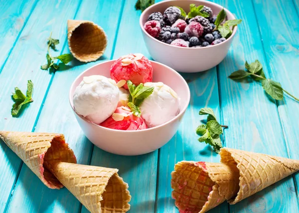Ice cream in bowl, berries and waffle cones on blue wooden table. Summer