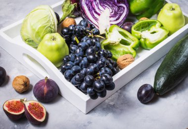 Taze organik çiğ yeşil ve mor renkli sebze ve meyve içinde karanlık taş zemin üzerine beyaz tepsi