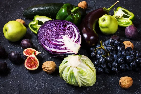 Färska ekologiska raw gröna och lila färgade grönsaker och frukter på mörk sten bakgrund — Stockfoto