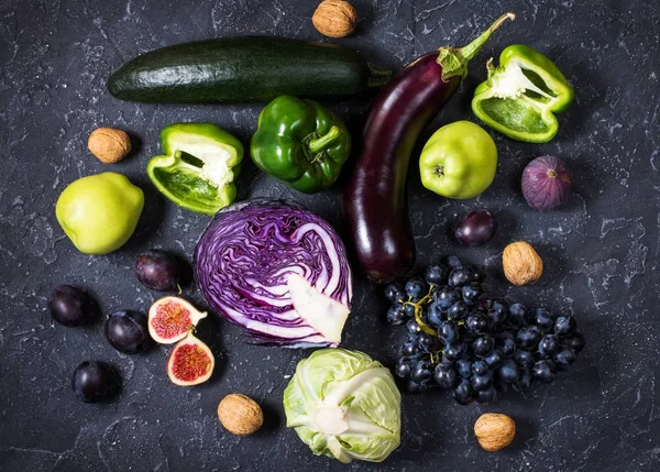 Fresh organic raw green and purple colored vegetables and fruits on dark stone background — Stock Photo, Image