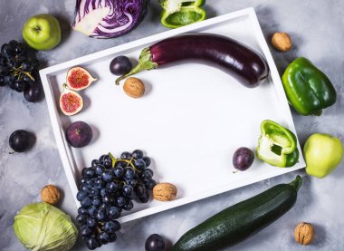 Taze organik çiğ yeşil ve mor renkli sebze ve meyvelerde taş zemin üzerine beyaz tepsi. Boşaltmak