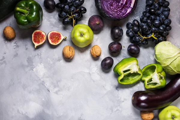 Färska ekologiska raw gröna och lila färgade grönsaker och frukter på sten bakgrund — Stockfoto