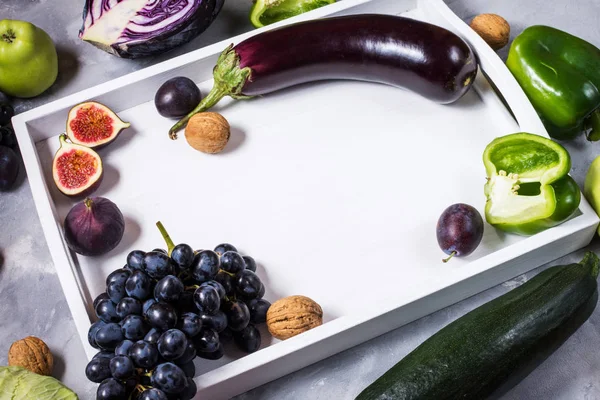 Verduras y frutas frescas orgánicas de color verde y púrpura en bandeja blanca sobre fondo de piedra. Espacio de copia —  Fotos de Stock