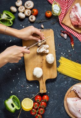 Kadınların elleri mantar kesti. Makarna malzemeler. Tavuk göğsü, Cherry Domates, spagetti makarna ve meyveleri koyu taş masanın üzerine