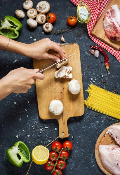 Kadınların elleri mantar kesti. Makarna malzemeler. Tavuk göğsü, Cherry Domates, spagetti makarna ve meyveleri koyu taş masanın üzerine