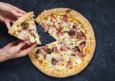 Eller siyah taş zemin üzerine Pizza Carbonara kesti. İtalyan Pizza Carbonara sosis, mantar ve peynir ile