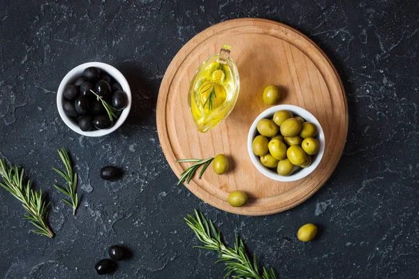 Black and green olives in wooden bowls on stone black background.