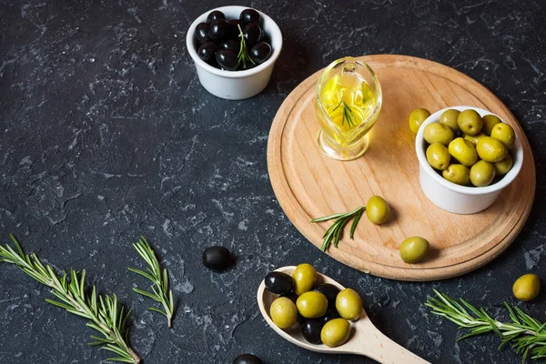 Black and green olives in wooden bowls on stone black background