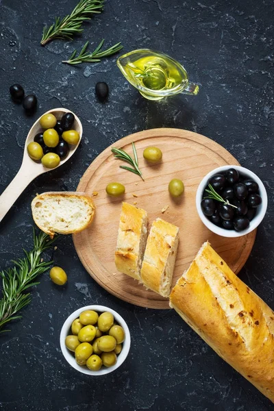 Black and green olives in wooden bowls on stone black background.