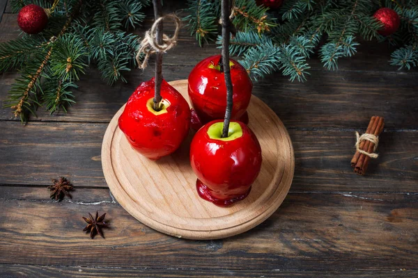 Red caramel apples on sticks on Dark wood background, with Christmas tree branches — Stock Photo, Image