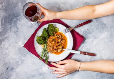 Sebze ve brokoli rustik beton zemin üzerine Dana gulaş, kadınların elleri kadeh şarap tutun..