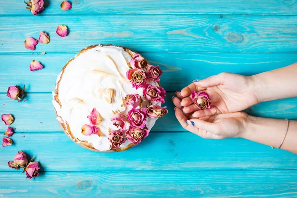 Woman's hands hold the dry rose. The white cream cake decorated dry rose on blue wood background. Top view.