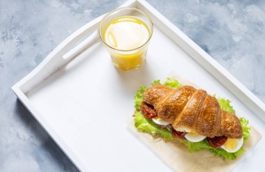 Ton balığı, katı pişmiş yumurta, salata ve güneşte kurutulmuş domates beyaz tepsi ile kruvasan sandviç. Bir bardak portakal suyu. Kahvaltı konsepti.