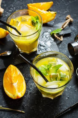 Portakal ve nane bardaklarda ve karanlık taş zemin üzerine soğuk alkollü yaz narenciye kokteylle. Araçlar, shaker, gözlük, nane yaprakları bar kokteyl yapımı.