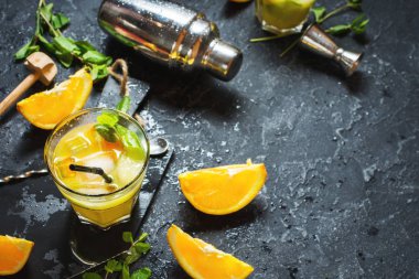 Portakal ve nane bardaklarda ve karanlık taş zemin üzerine soğuk alkollü yaz narenciye kokteylle. Araçlar, shaker, gözlük, nane yaprakları bar kokteyl yapımı.
