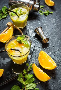 Portakal ve nane bardaklarda ve karanlık taş zemin üzerine soğuk alkollü yaz narenciye kokteylle. Kokteyl araçları yapımı, shaker, nane yaprakları.