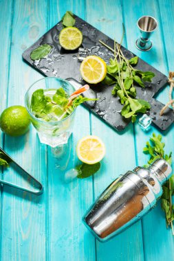 Mojito kokteyl limon ve nane highball cam üzerinde mavi bir ahşap masa. İçki yapım araçları ve kokteyl için malzemeler