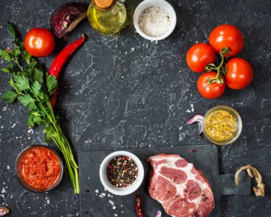 Karanlık taş arka plan üzerinde yemek pişirmek için malzemelerle çiğ mermer et biftek.