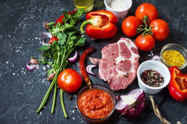 Karanlık taş arka plan üzerinde yemek pişirmek için malzemelerle çiğ mermer et biftek.