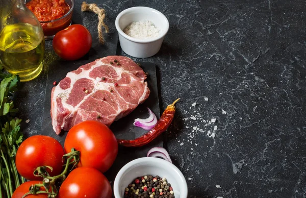 Karanlık taş arka plan üzerinde yemek pişirmek için malzemelerle çiğ mermer et biftek