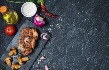 Sulu domuz biftek baharat ve ızgara mushroomson koyu taş arka plan ile. Üstten Görünüm