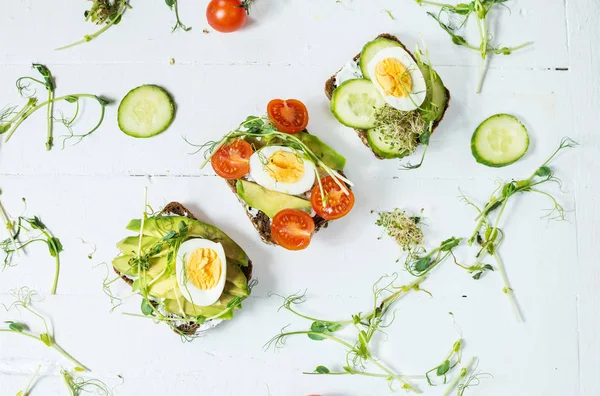 Tasty sandwiches with egg, avocado and vegetables on wooden white rustic background. Flat lay