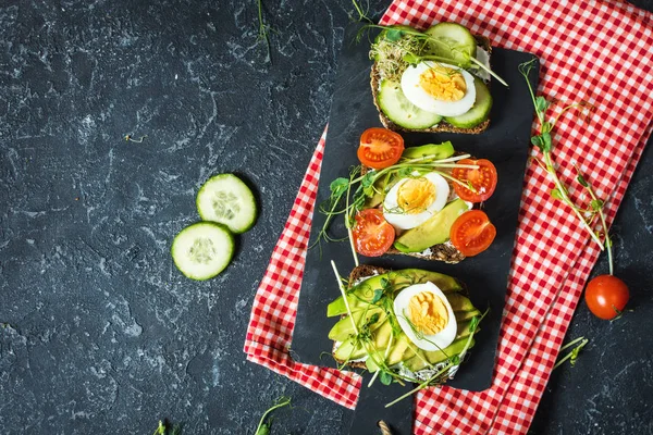 Tasty sandwiches with egg, avocado and vegetables on stone black background. Copy