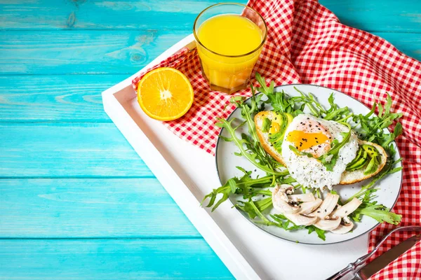 Смачний бутерброд з авокадо та яйцем, рукола на білому фоні лотка на синьому дереві. сніданок — стокове фото