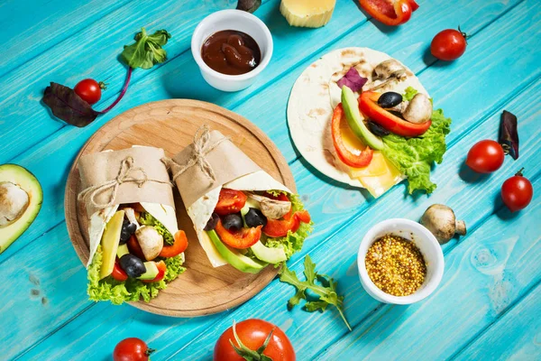 Hälsosam vegansk lunch mellanmål. Tortilla wraps med champinjoner, färska grönsaker och råvaror på blå trä bakgrund — Stockfoto