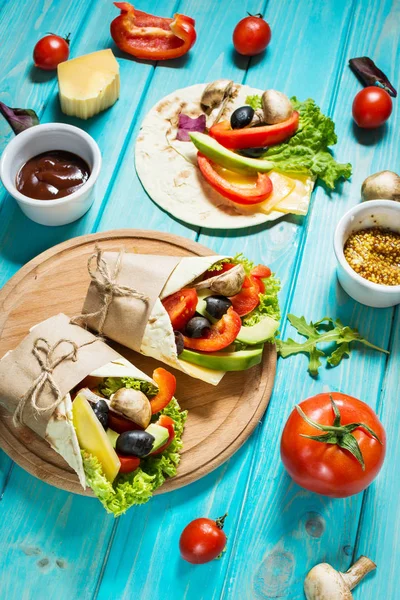 Hälsosam vegansk lunch mellanmål. Tortilla wraps med champinjoner, färska grönsaker och råvaror på blå trä bakgrund — Stockfoto