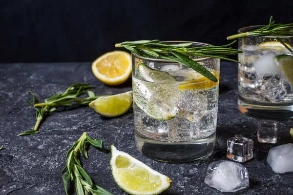 Alcoholic drink gin tonic cocktail with lemon, rosemary and ice on stone table