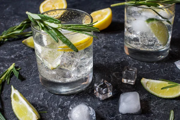 Bebida alcohólica gin tonic cóctel con limón, romero y hielo en la mesa de piedra —  Fotos de Stock