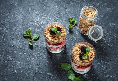 Sağlıklı katmanlı tatlı yoğurt, granola, reçel, böğürtlen cam taş zemin üzerine.