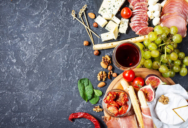 Italian antipasto with prosciutto, ham, cheese, olives and grissini breadsticks on black stone background.