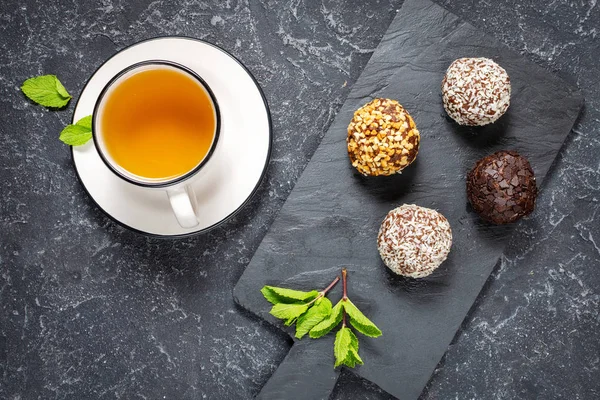 Xícara de chá quente com hortelã e doces no fundo de pedra preta — Fotografia de Stock