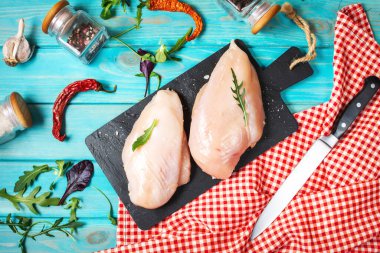 Taze çiğ tavuk filetosu, baharatlar ve otlar mavi ahşap arka planda.