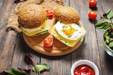 İki hamburger, tavuk, sade ahşap arka planda kızarmış yumurta ve peynir.
