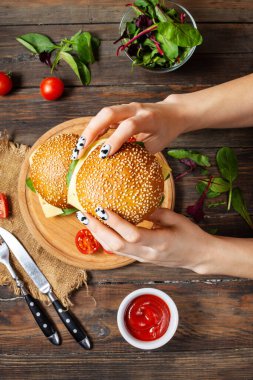 Kadın eli, ahşap arka planda tavuk, sahanda yumurta ve peynirli bir burger tutuyor. Üst görünüm