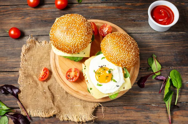 Breakfast two burgers with chicken, fried egg and cheese on a rustic wooden background