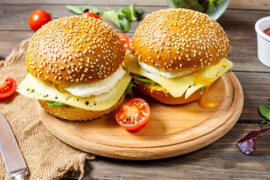 İki hamburger, tavuk, sade ahşap arka planda kızarmış yumurta ve peynir.
