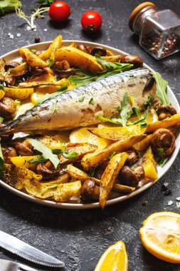 Limonlu fırında uskumru, fırında patates ve mantarlı siyah taş zemin üzerinde bir tabak. Kapat.