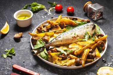 Limonlu fırında uskumru, fırında patates ve mantarlı siyah taş arka planda bir tabak..