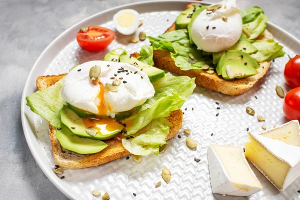 Healthy sandwich - poached eggs and avocado on toast with tomatoes on concrete background.