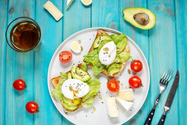 Healthy sandwich - poached eggs and avocado on toast with tomatoes on blue wooden background. Top view