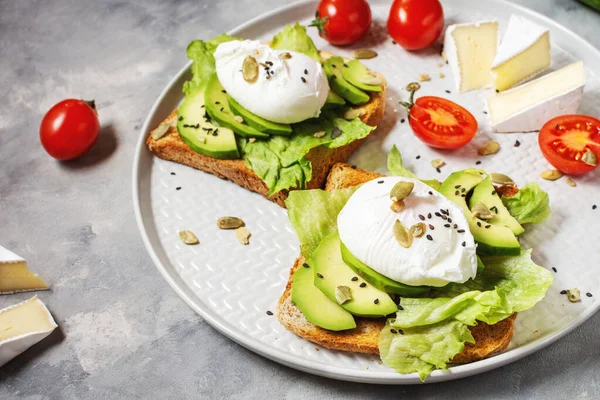 Healthy sandwich - poached eggs and avocado on toast with tomatoes on concrete background. Close up