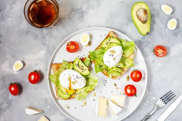 Healthy sandwich - poached eggs and avocado on toast with tomatoes on concrete background. Top view