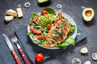 Izgara tavuk göğsü ve ıspanaklı avokado salatası ve siyah taş arka planda vişneli domates. Sağlıklı yemek, ketojenik diyet, öğle yemeği konsepti..
